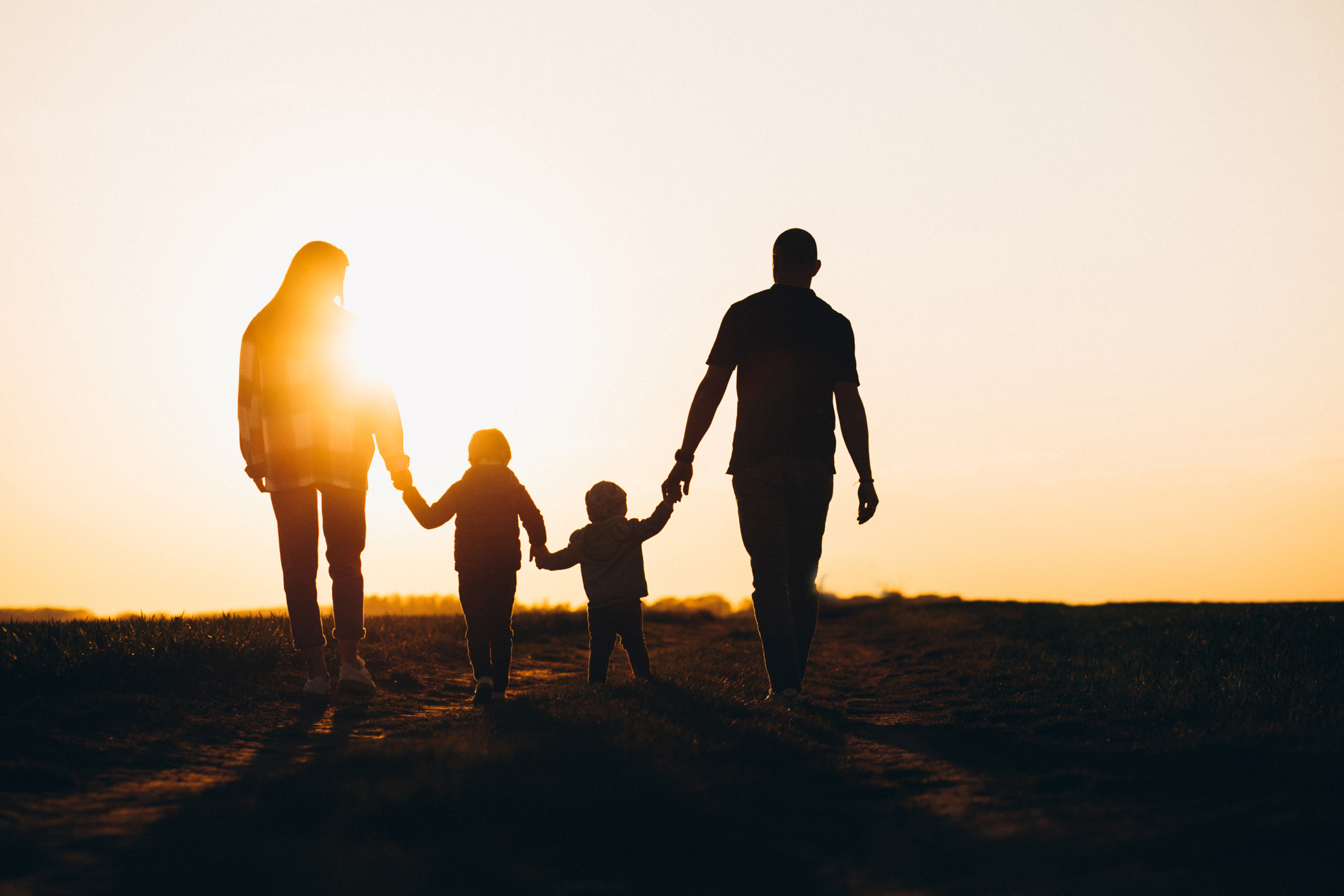 Familie går hånd i hånd i solnedgangen